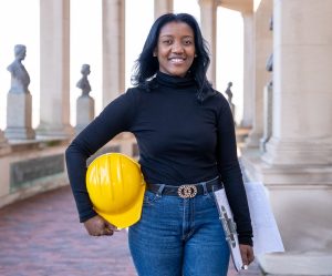 Architect Lilian Romero stands in the Hall of Fame with hat and clipboard