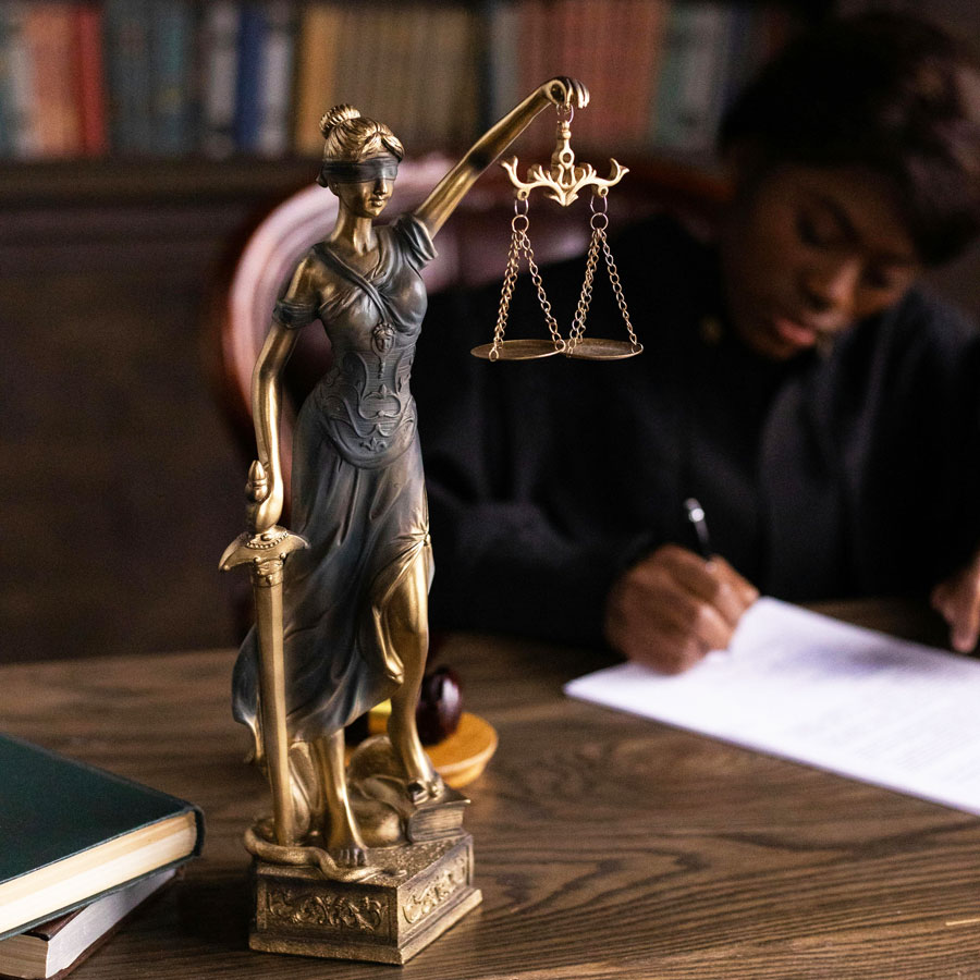 Image of judge at a desk which has on it a figurine of the mythical figure Justice holding scales